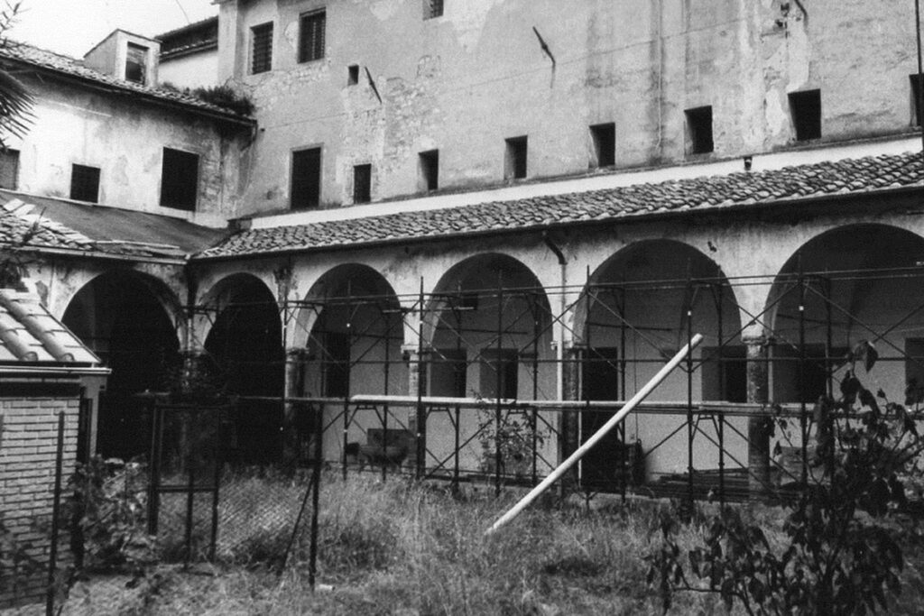 Veduta storica in bianco e nero del chiostro interno del complesso di San Domenico a San Gimignano con ponteggi di cantiere e arcate originali